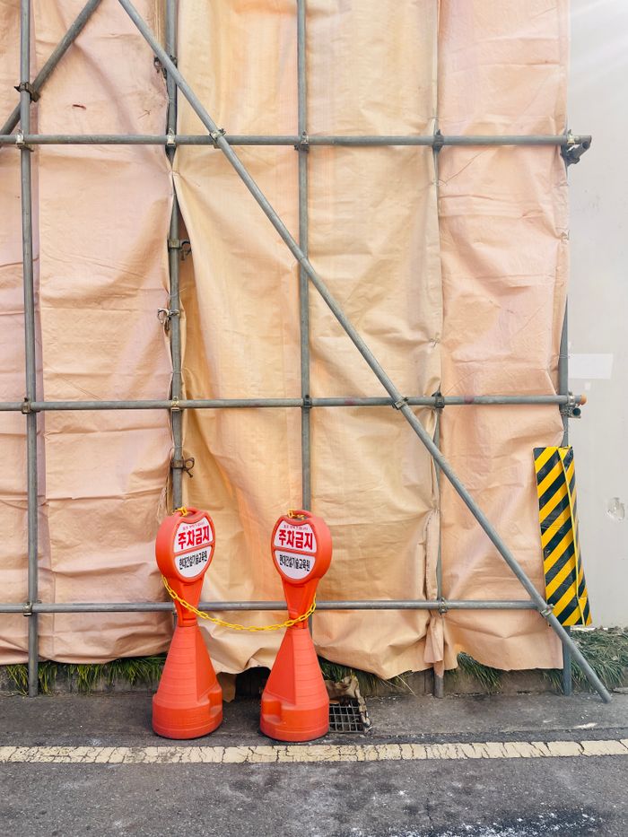 Image of a construction site in Seoul, featuring bright orange traffic cones and scaffolding.