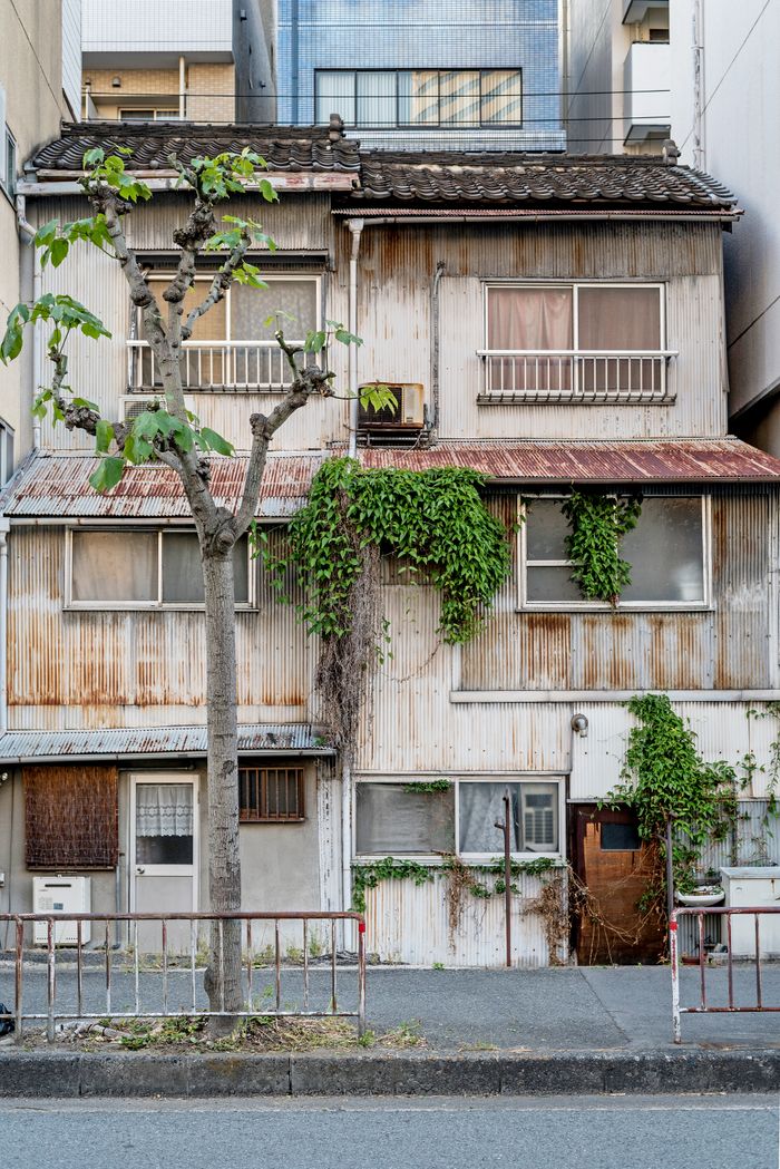 A rustic abandoned building with vines on a street in Japan, showcasing urban decay.